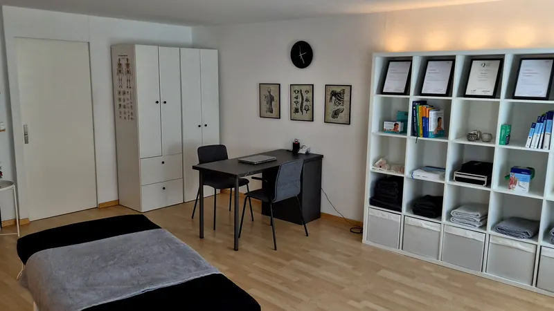 Behandlungsraum mit Liege, Schreibtisch und Regal